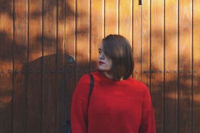 Young woman standing against wooden wall