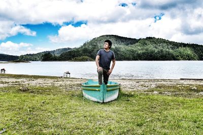 Man standing in boat moored on field by lake against sky