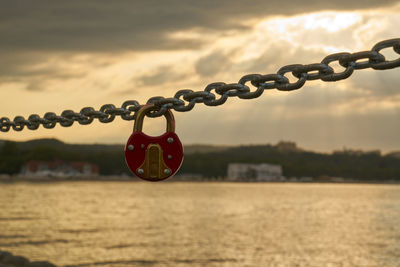 Close-up of lock attached to chain against sea at sunset