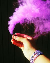 Cropped hand holding bomb emitting purple smoke