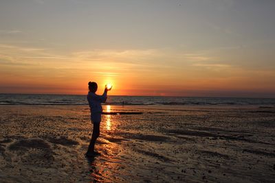 Silhouette man standing on beach against sky during sunset