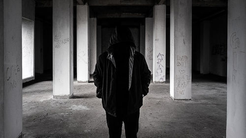 Person in hooded shirt standing at abandoned building