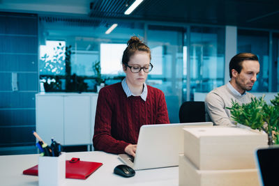 Businesswoman using laptop while sitting by colleague at desk in creative office