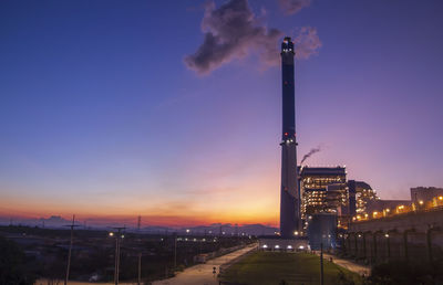 Illuminated factory against sky at dusk