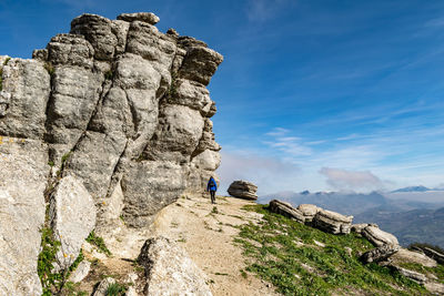 Rear view of woman walking on rock formation against sky