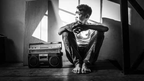 Thoughtful young man sitting by radio on floor at home