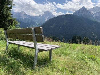 Empty bench on field against mountains