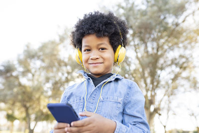 Portrait of smiling boy using mobile phone against trees