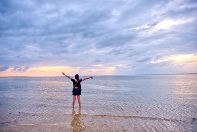 Rear view of woman with arms outstretched standing at beach during sunset