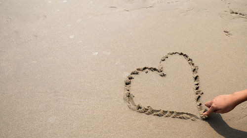 The hand of a woman drawing hearts in the sand on the beach