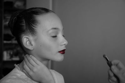 Close-up of girl with eyes closed applying red lipstick against wall