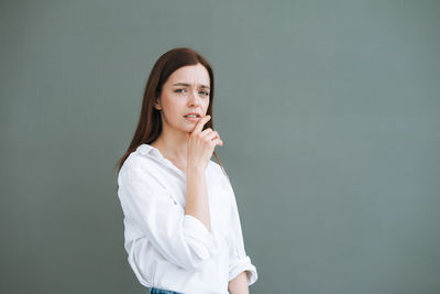 Young unhappy woman with long hair in white shirt on grey background, negative emotion