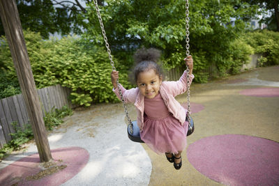 Happy girl having fun on swing in playground