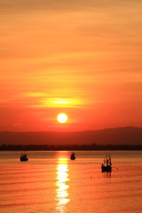 Silhouette boats sailing in sea against orange sky