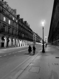People walking on road by buildings against sky in city