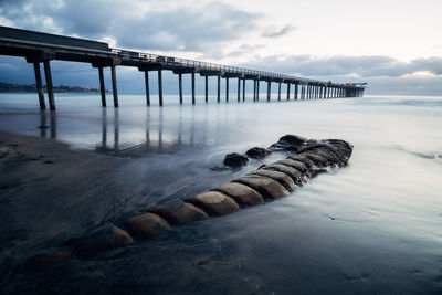 Pier on sea against cloudy sky during sunset