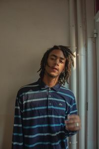 Portrait of young man standing against wall at home