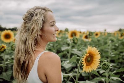 Smiling young woman amidst sunflowers against sky