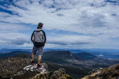 Rear view of man standing on rock against sky