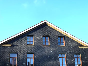 Low angle view of black stone layers on facade building against blue sky