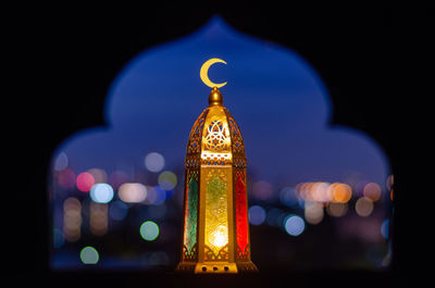 Lantern that have moon symbol on top with blurred focus of paper cut for mosque shape background.