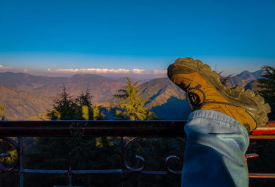 Rear view of woman looking at view of mountain against blue sky