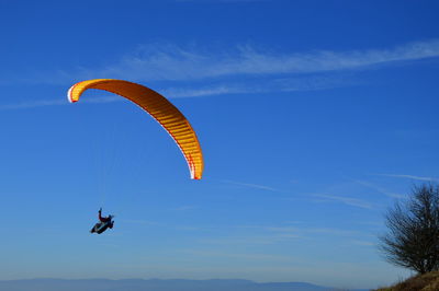 Low angle view of person paragliding against blue sky