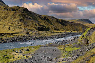 Beautiful stream flowing amidst mountains at seljavellir against cloudy sky