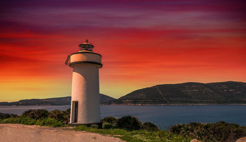 Lighthouse by sea against orange sky