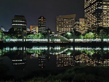 Illuminated buildings by river in city against sky at night