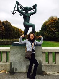 Full length of young woman standing by statue against sky