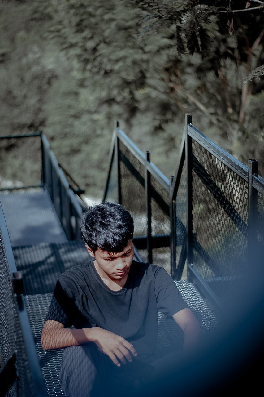 one person, railing, adult, blue, men, young adult, nature, staircase, front view, water, sitting, outdoors, portrait, architecture, day, glasses, lifestyles, casual clothing, leisure activity, high angle view