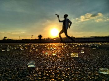 Silhouette man holding gun while standing on road against sky during sunset