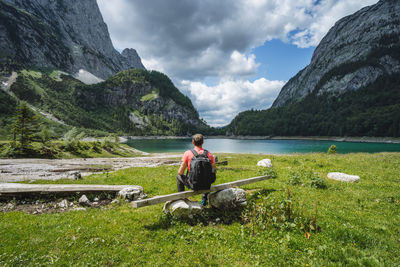 Man sitting on grass by lake against sky