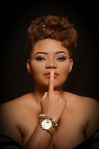 Portrait of sensuous woman with finger on lips against black background