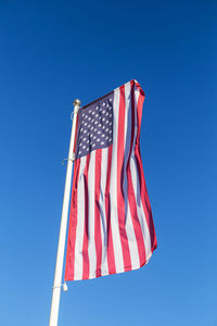 The american flag flies against a clear blue sky, vertical. freedom and independence concept. 