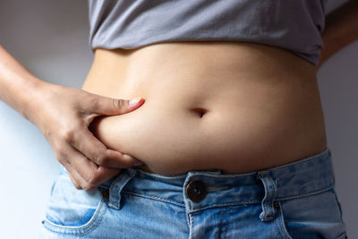 Midsection of woman holding abdomen while standing against gray wall