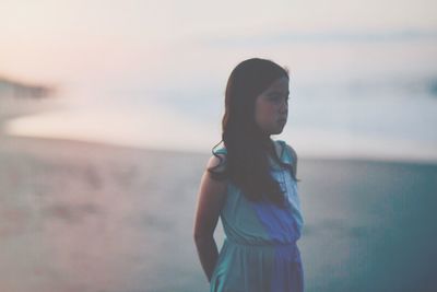 Young woman standing at beach against sky during sunset