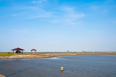 Pavilions by lake against blue sky.