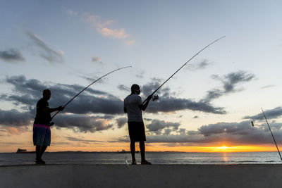 Man fishing on beach against sky during sunset