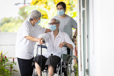 People standing by man sitting on wheelchair wearing mask