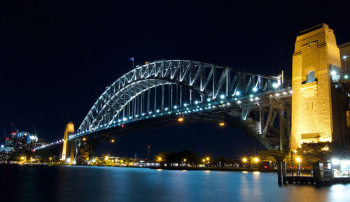 Illuminated sydney harbour bridge over bay of water in city at night