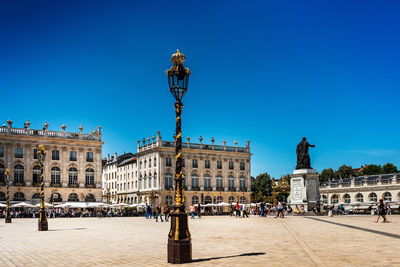 People walking on town square by statue against sky