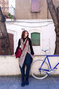 Young woman leaning on a city wall with vintage bike in sunny day