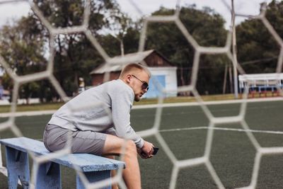 Side view of man sitting on bench seen through net