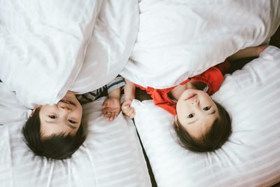 High angle portrait of siblings relaxing on bed at home