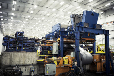 Metal sheets being rolled up on machines at factory against illuminated ceiling