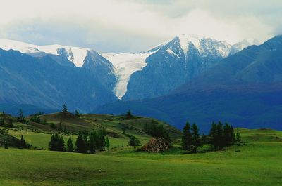 Scenic view of grassy field and mountains against cloudy sky