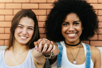 Portrait of smiling friends holding hands against brick wall