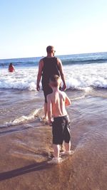 Full length of shirtless man standing at beach against sky